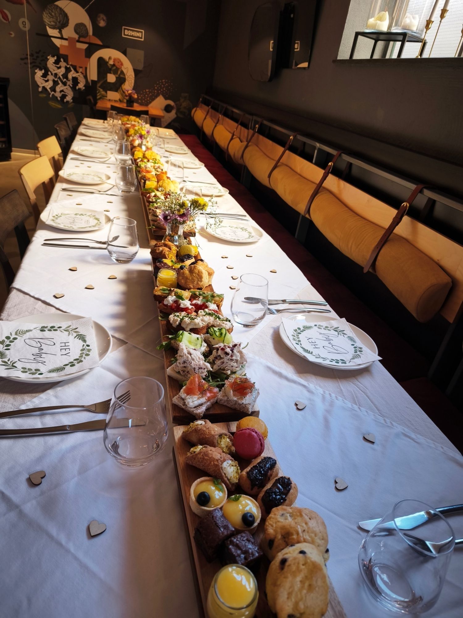 A long table set for an Afternoon Tea event, with boards of finger sandwiches, scones, cannoli, macarons and lemon tarts down the middle