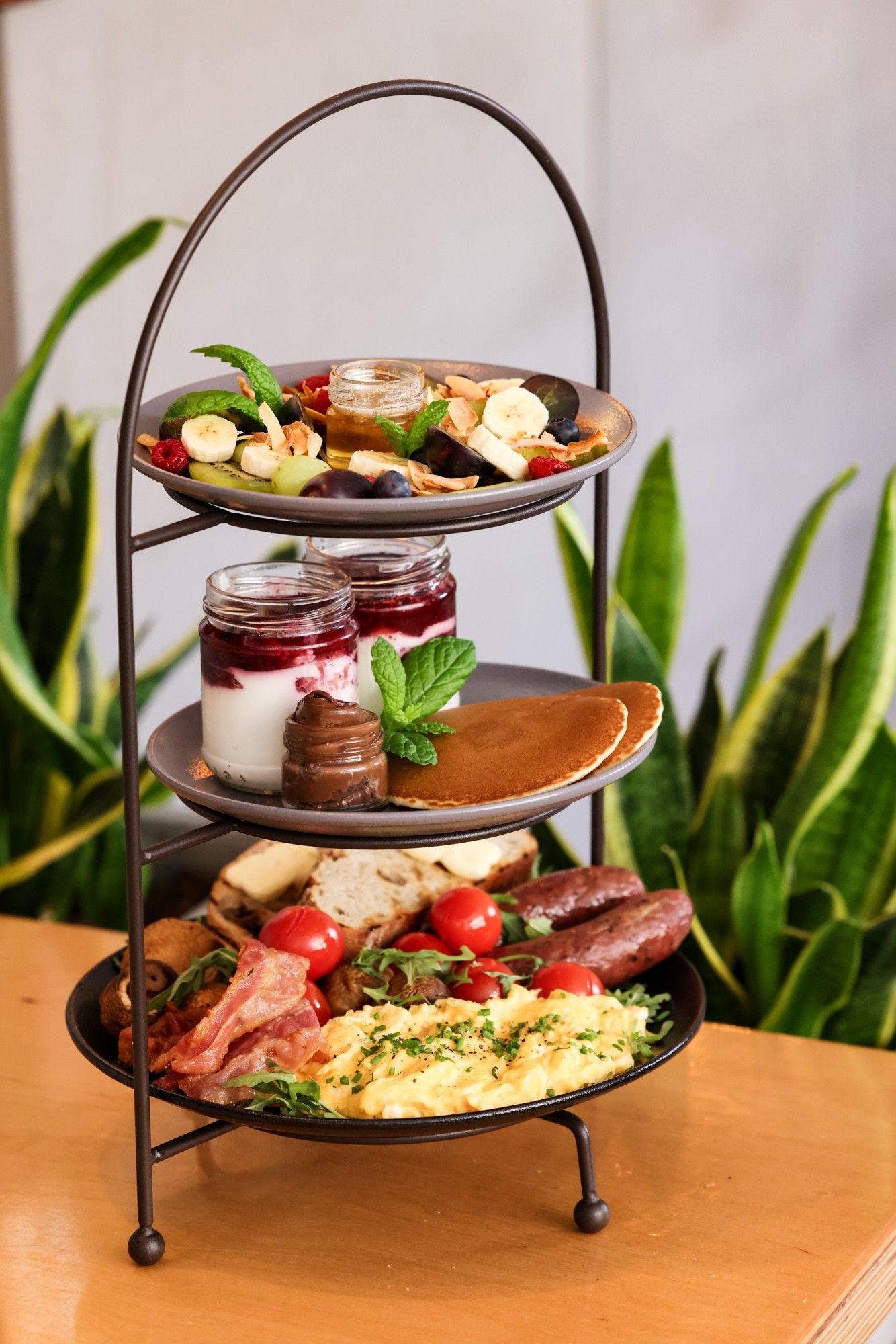 The Ultimate Breakfast Feast on a three-tier stand: fruit, yoghurt pots and pancakes above scrambled eggs, bacon, sausages and sourdough