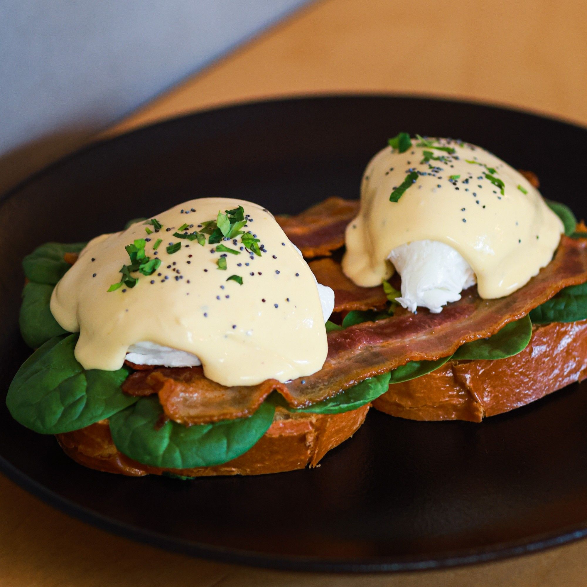 Uova alla Benedict con bacon croccante, spinaci, salsa olandese e semi di papavero su brioche tostata