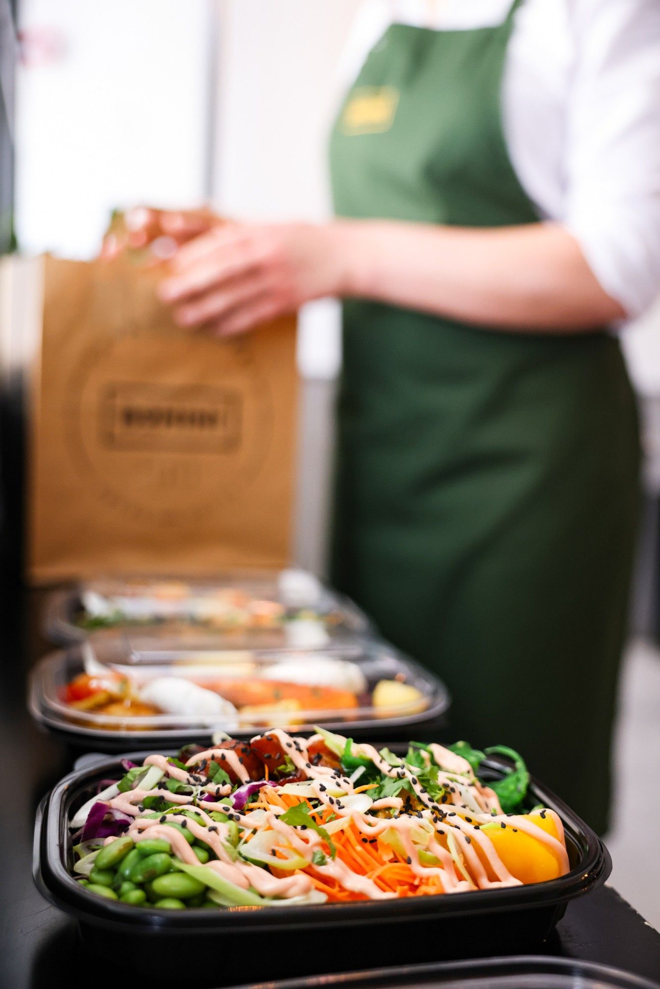 A poke bowl and takeaway boxes lined up beside a Bohini paper bag, ready for delivery