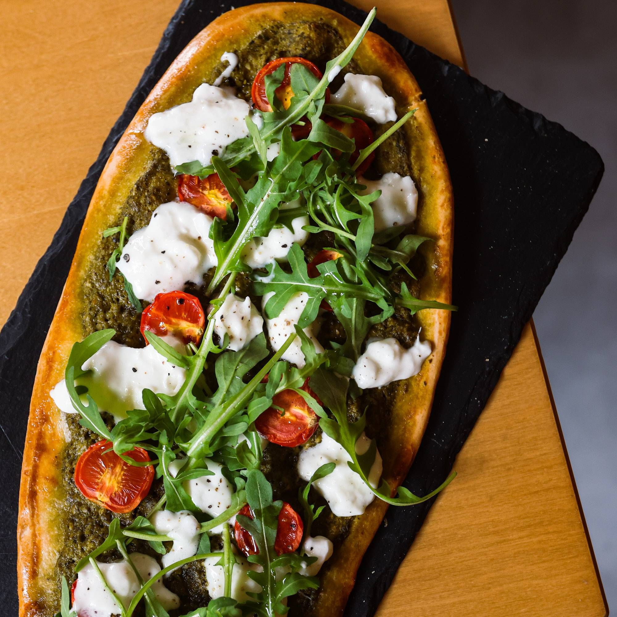 Focaccia al pesto di basilico con pomodorini arrosto, rucola e burrata su un tagliere di ardesia