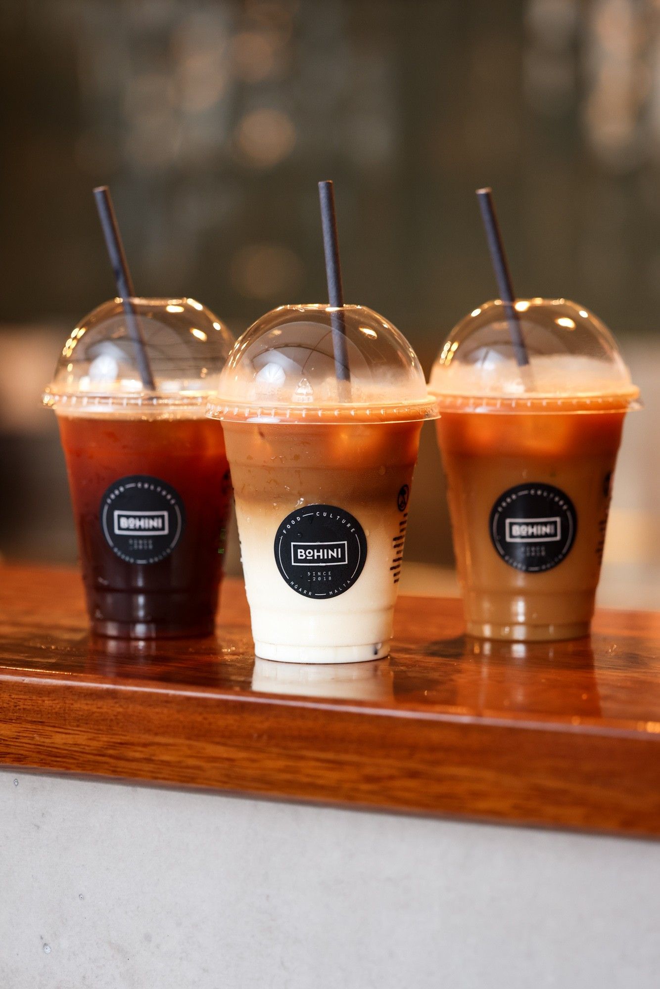 Three iced coffees in Bohini-branded cups on a wooden bar
