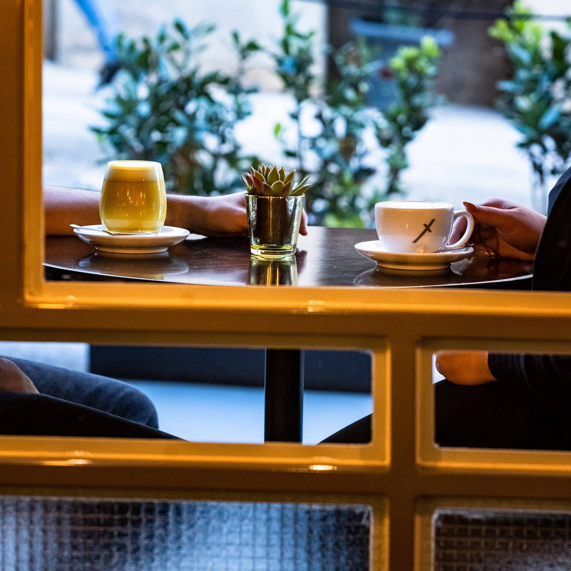 Two guests with a turmeric latte and a cappuccino at a window table inside Bohini